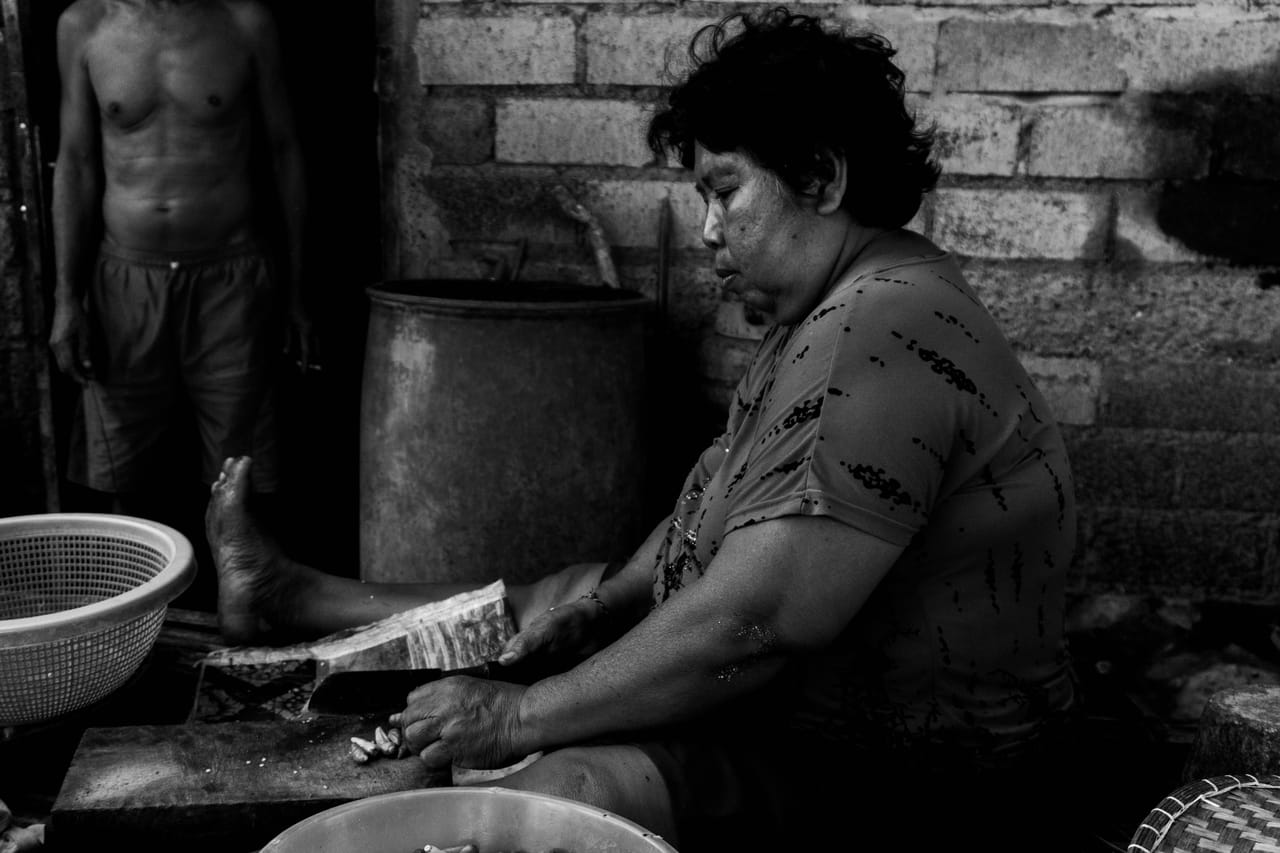Rotenese woman cooking outdoors for a village gathering, simple pots in the late afternoon