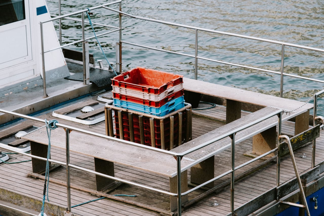 Crates and sacks stacked in three groups on a wooden harbor dock beside the sea