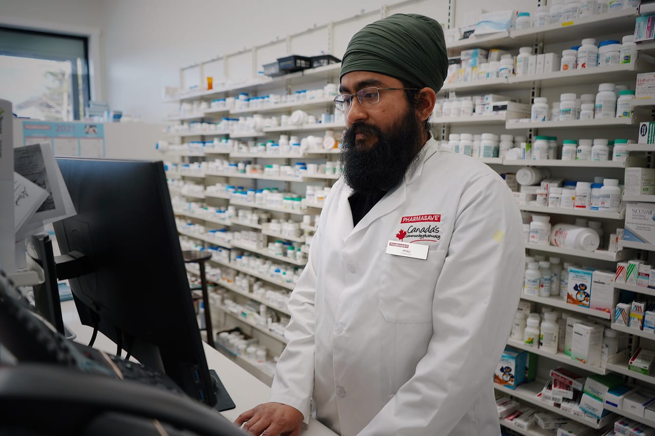 Local pharmacist behind the counter of a small island pharmacy with limited medication shelves