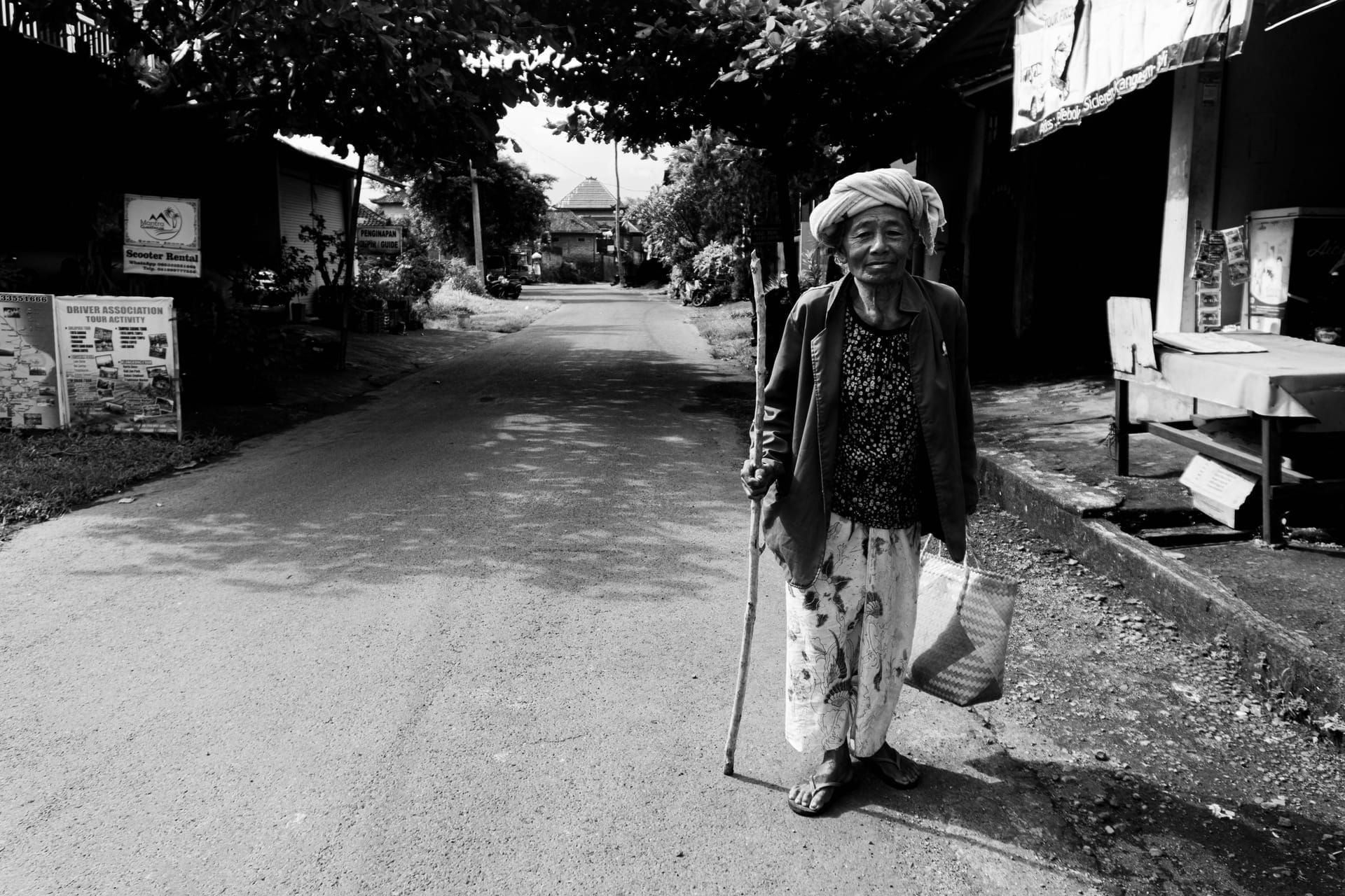 An elderly Rotenese woman offering a betel nut bundle from a wooden box to a guest inside a home on Rote