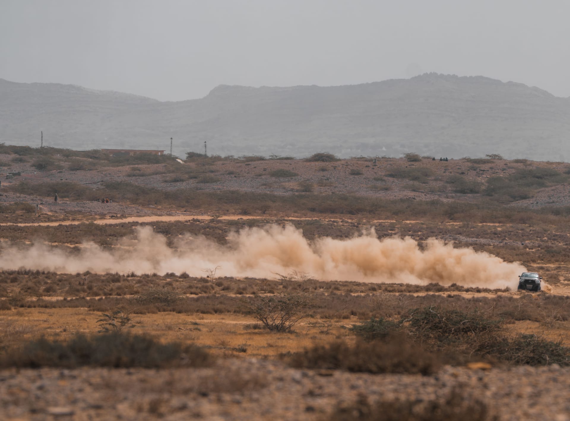 A dusty red dirt road on Rote Island during the dry season, with pale straw hills and dust rising behind a passing truck