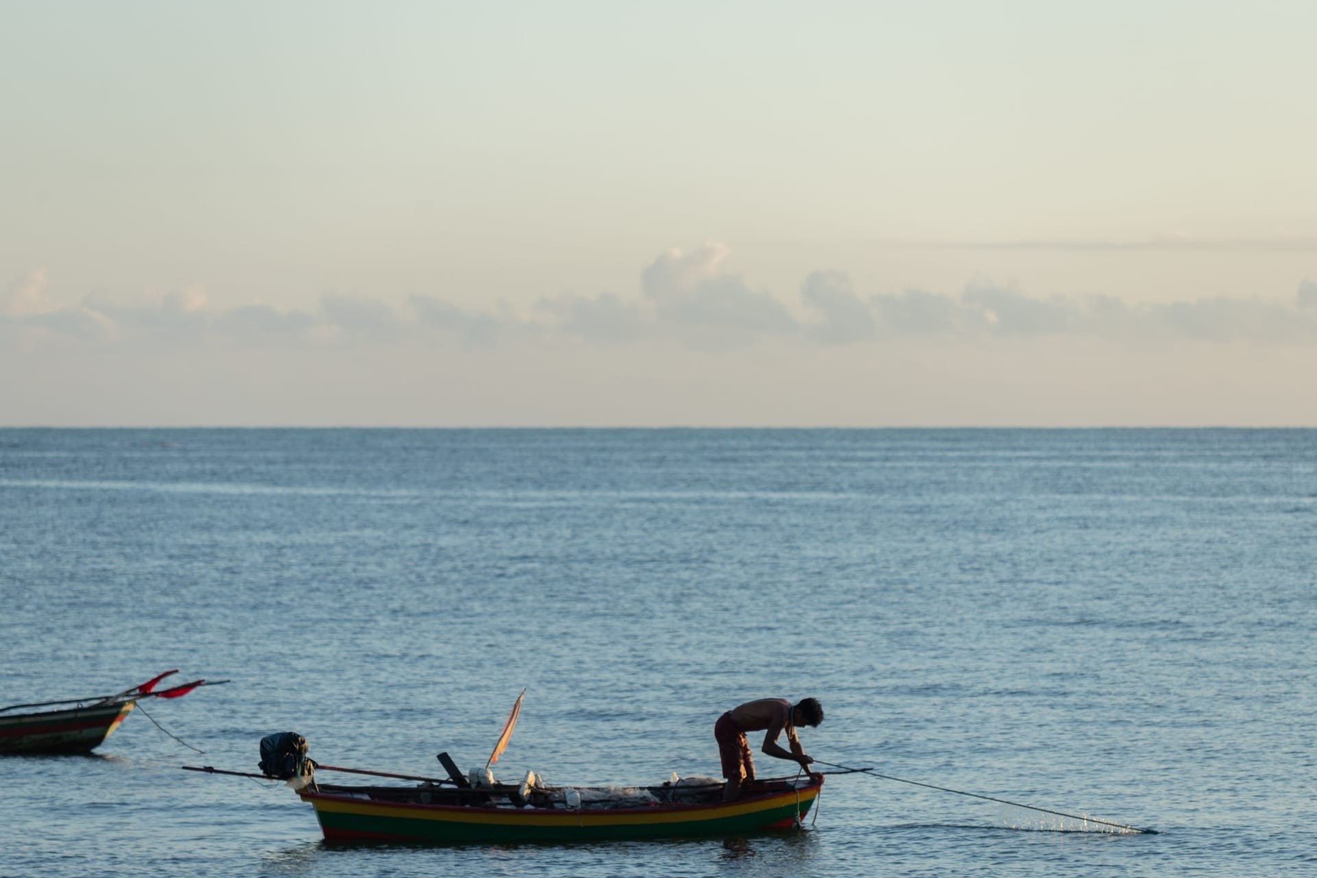 Local captain steering a wooden fishing boat carrying surfers out to an offshore reef break at dawn on Rote