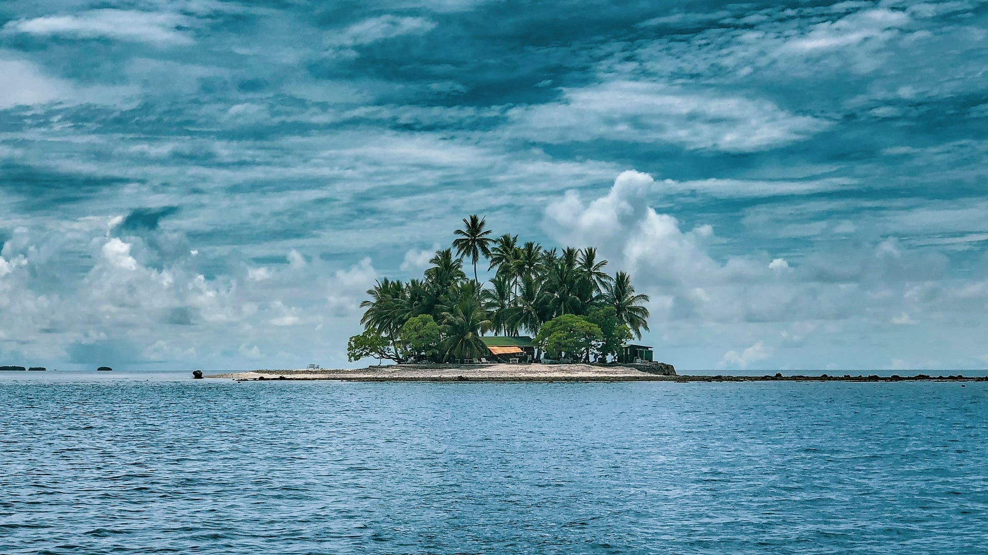 A hand pointing across open water toward a distant, hazy island on the horizon