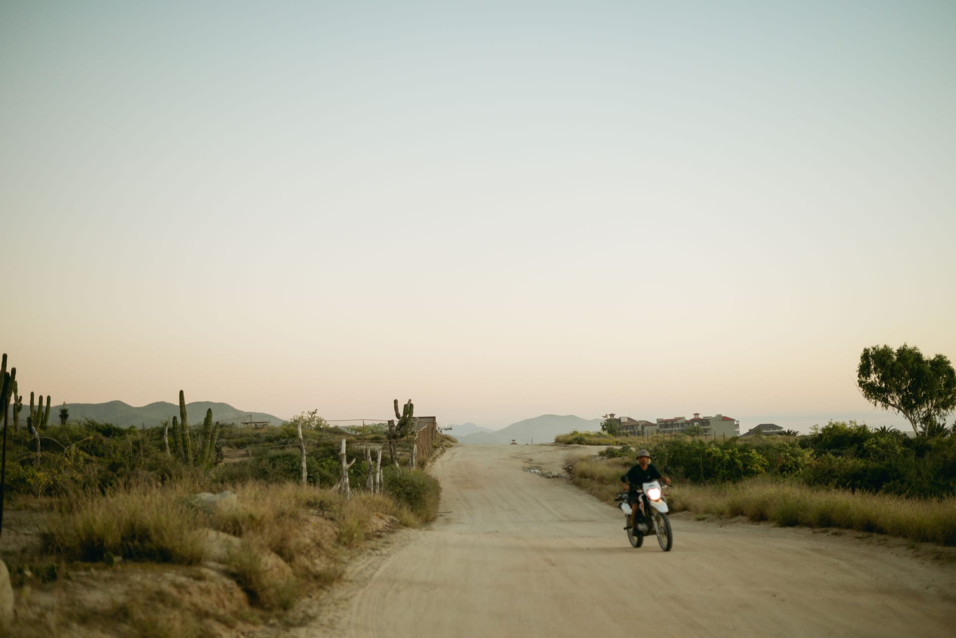 Traveler riding a motorbike along an empty dirt road across Sumba island at dawn