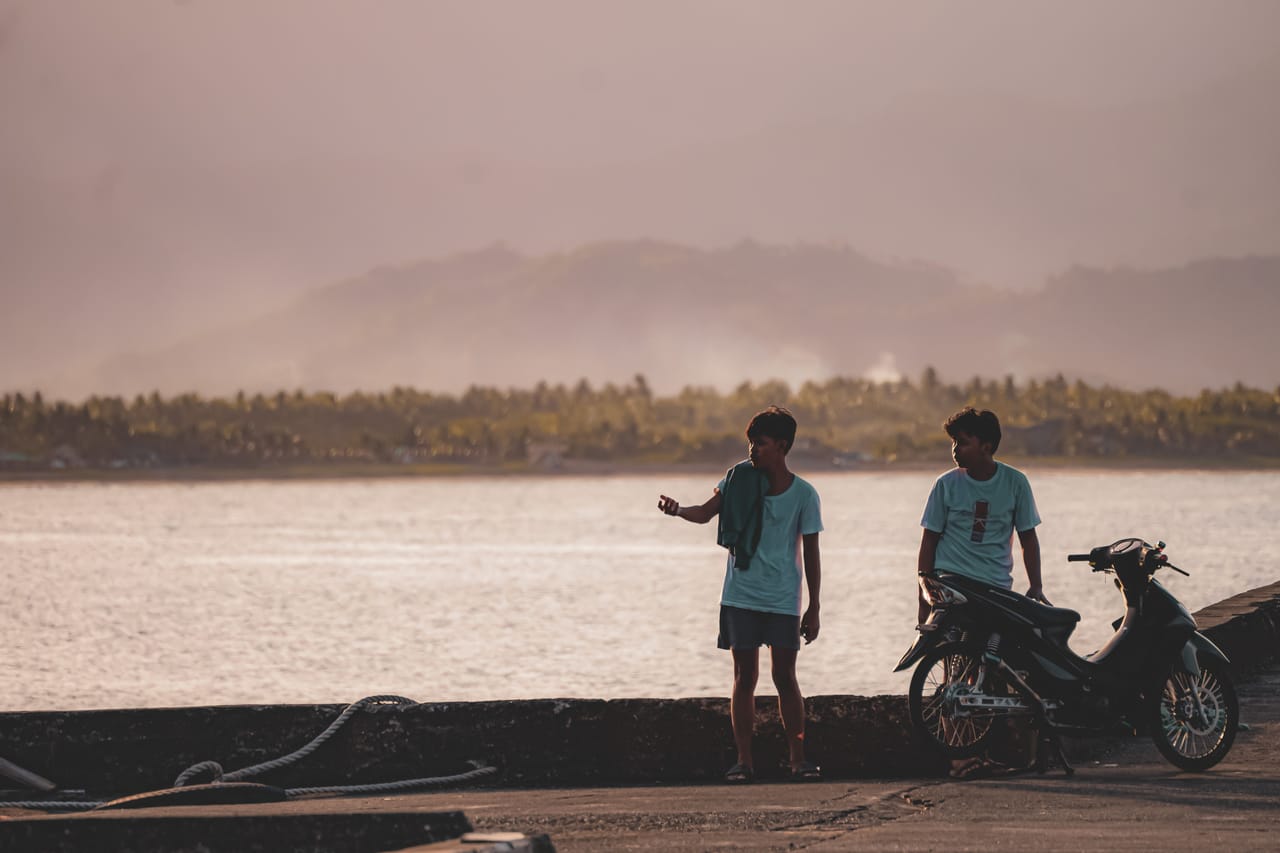 A local landlord and a long-stay tenant talking outside a simple home on Rote, a motorbike parked beside them