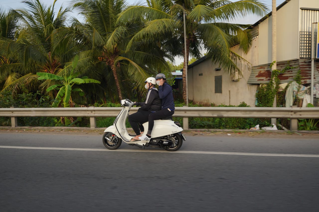 A foreigner riding a motorbike along a dirt road past beachfront land and palms on Rote