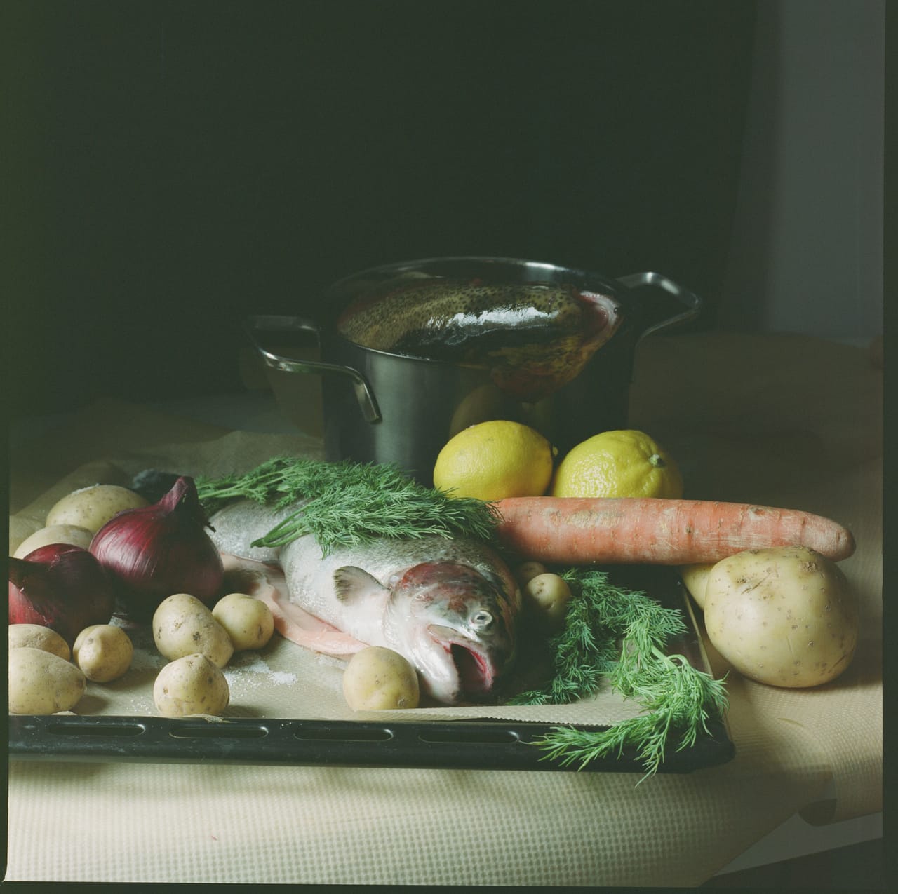 Fresh whole fish laid out next to bundles of greens, chilli and shallots on a stall
