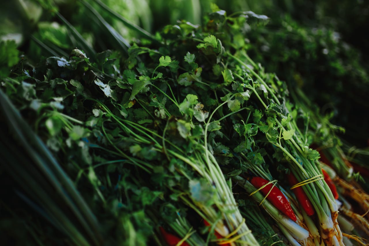 Greens tied in bunches and tomatoes and chillies grouped into small piles on a mat