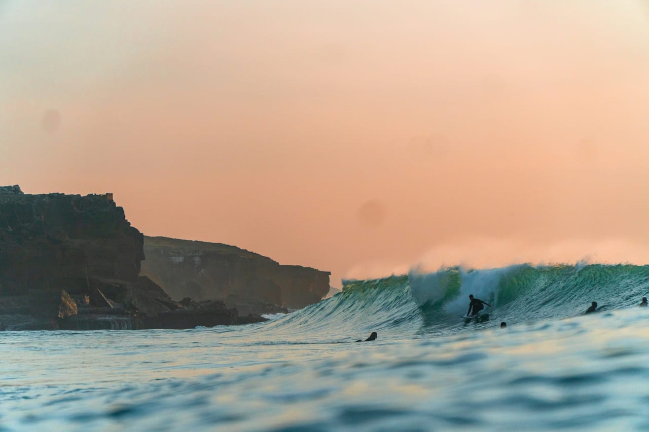 A handful of surfers waiting in the water at an empty reef break under soft dawn light