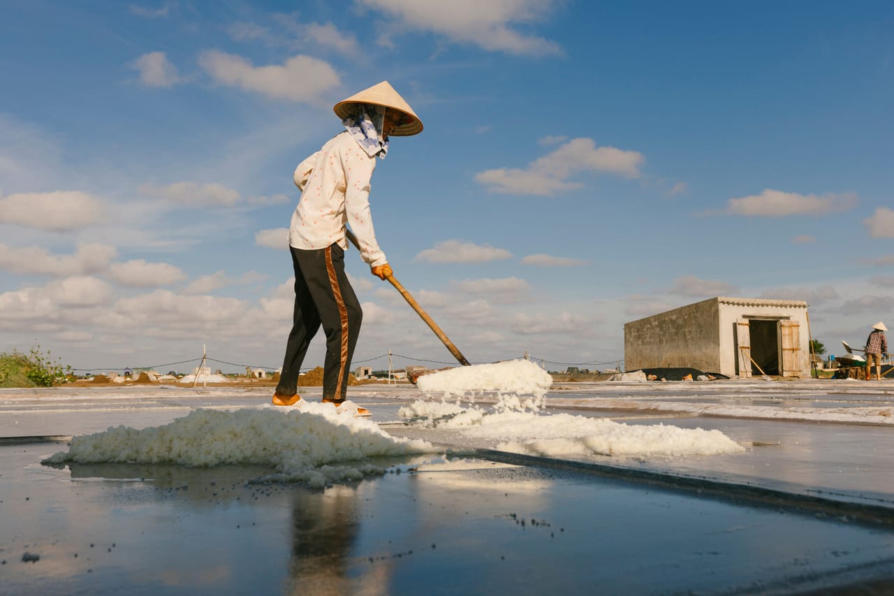 Rotenese worker raking salt by hand in a drying pan on Rote Island