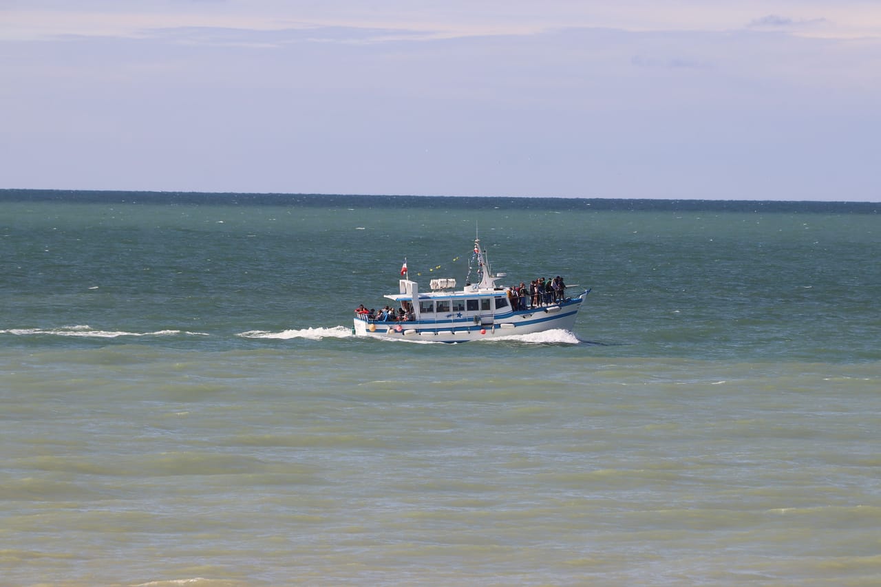 A small wooden boat crossing open water toward a distant low island