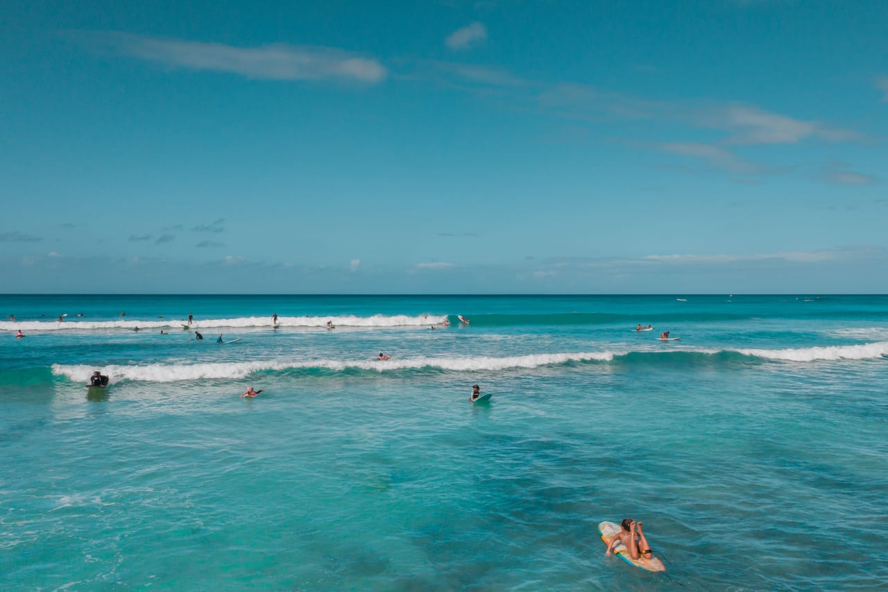 Surfers spread across the sections of a long reef lineup, one taking off at the peak while others wait