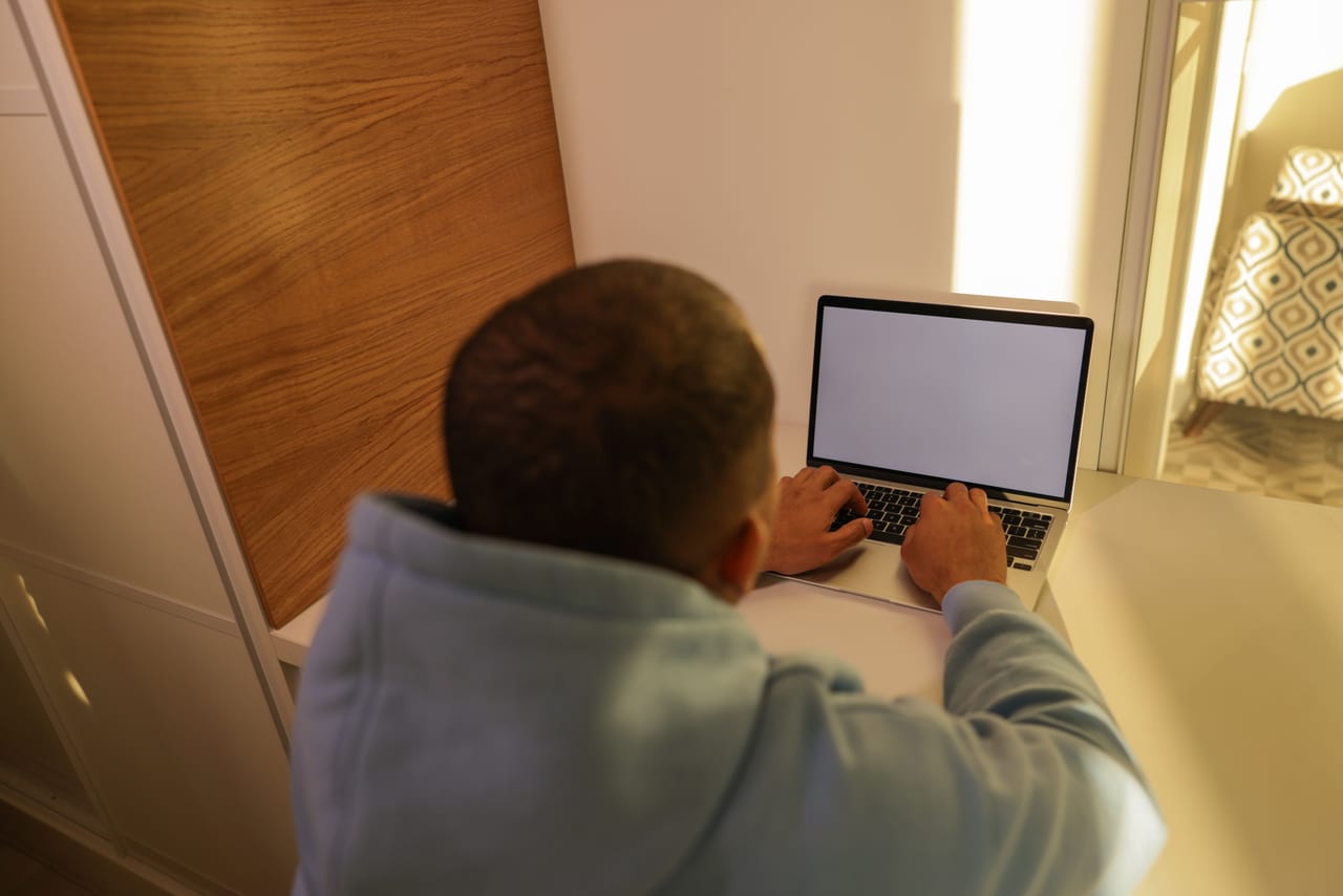 Person working on a laptop in a simple open-air Rote home during quiet morning hours